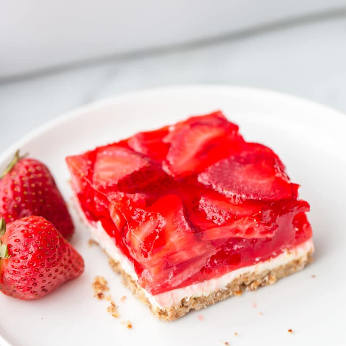 Pretzel salad recipe on white plate with strawberries on the side.