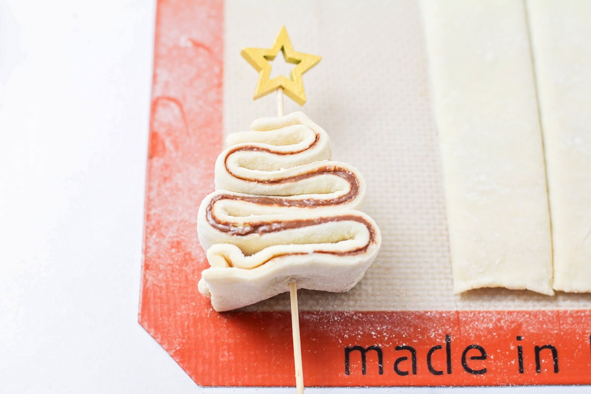 Shaping puff pastry into a Christmas tree on a skewer.