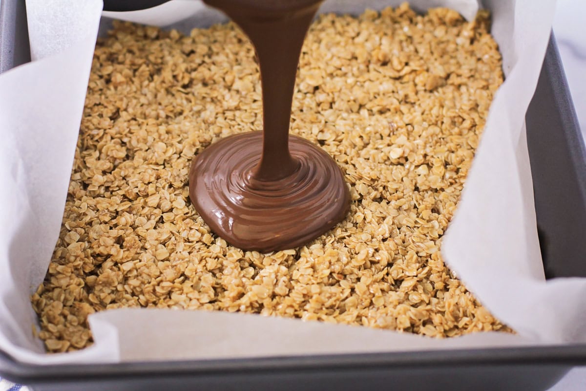 Chocolate being poured over oat layer.