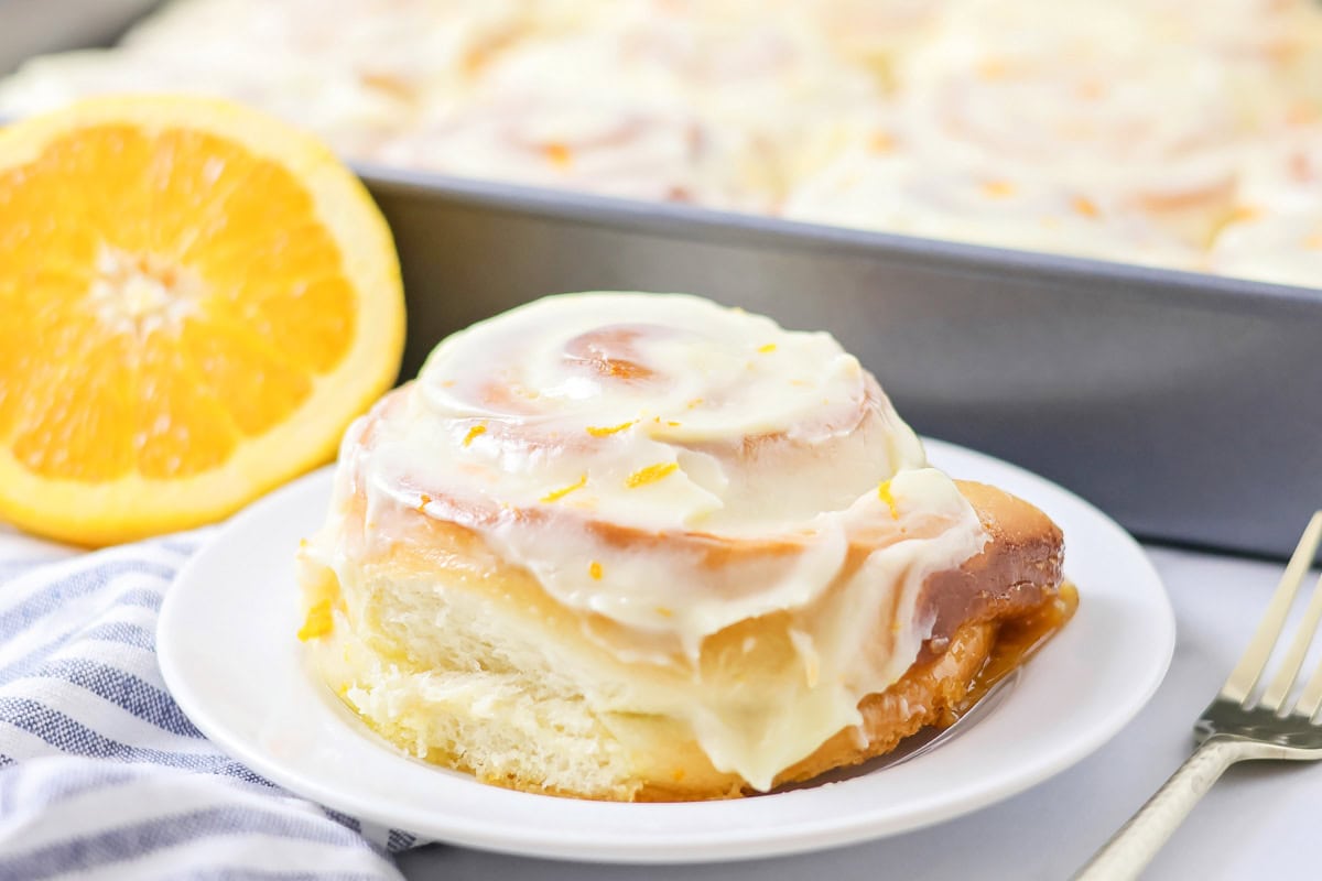 Filled with orange zest and smothered in an irresistible lemon frosting, these orange rolls are citrus-sweet roll heaven! An orange roll on a white plate.