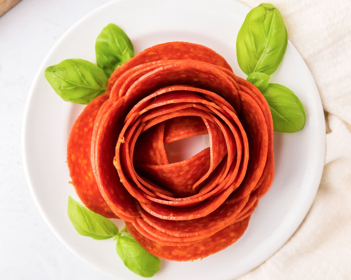 A pepperoni rose on a white plate.