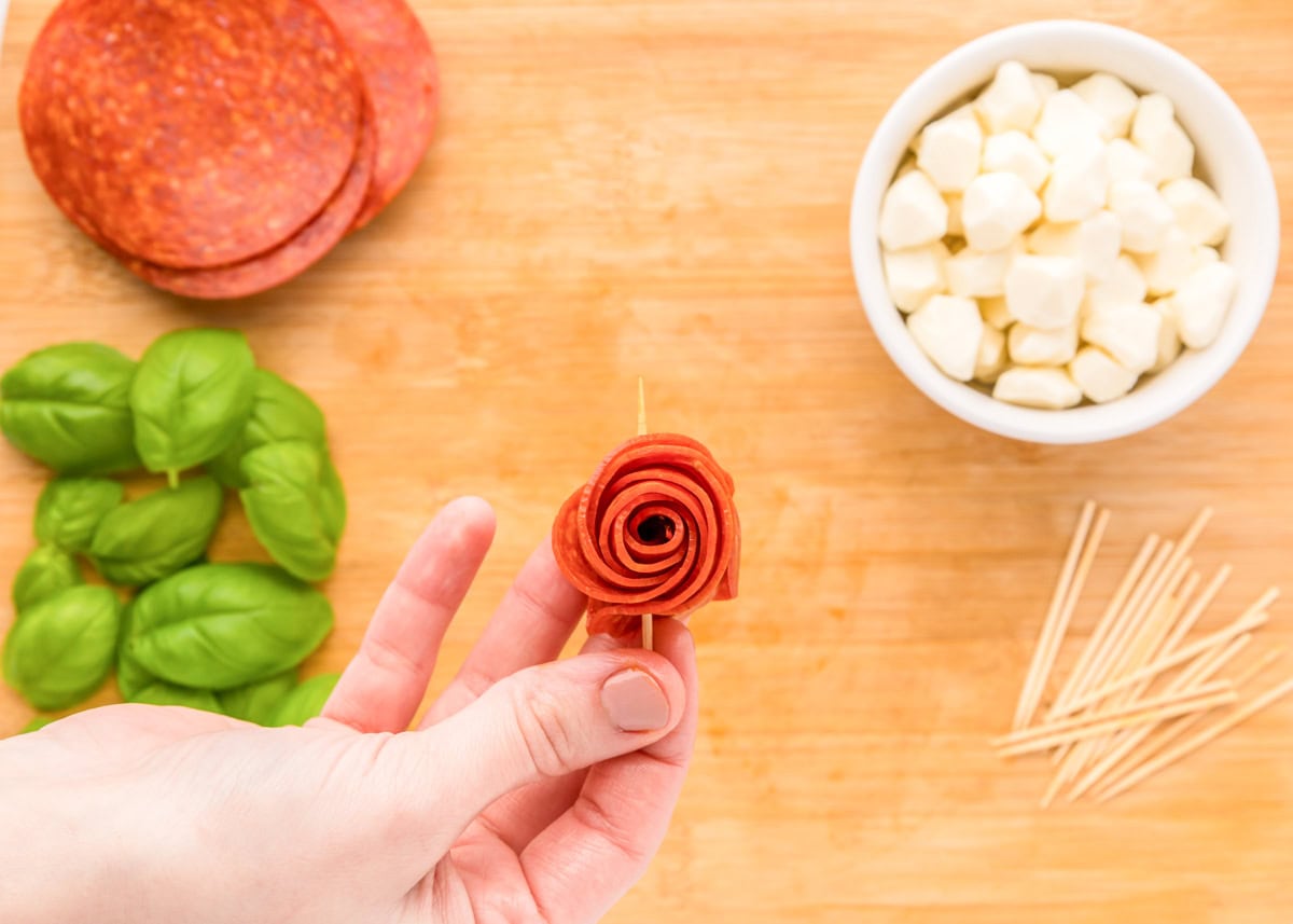 Pushing a skewer through a rolled pepperoni flower.