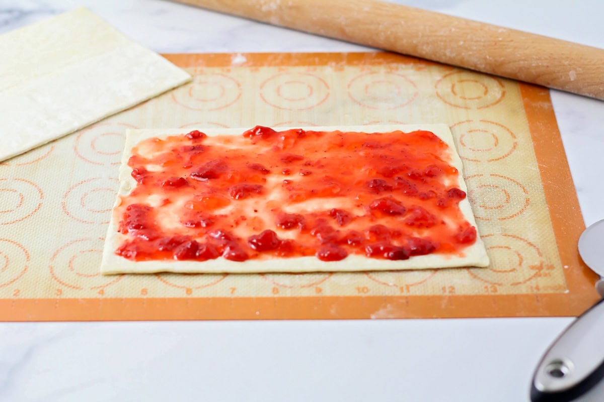 Spreading strawberry jam on puff pastry sheet.