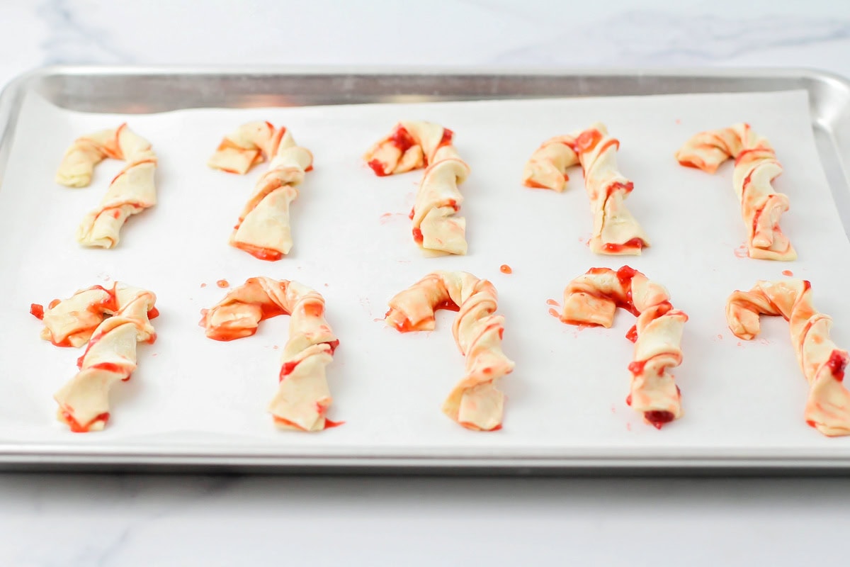 Candy cane shaped puff pastries on a lined baking sheet.