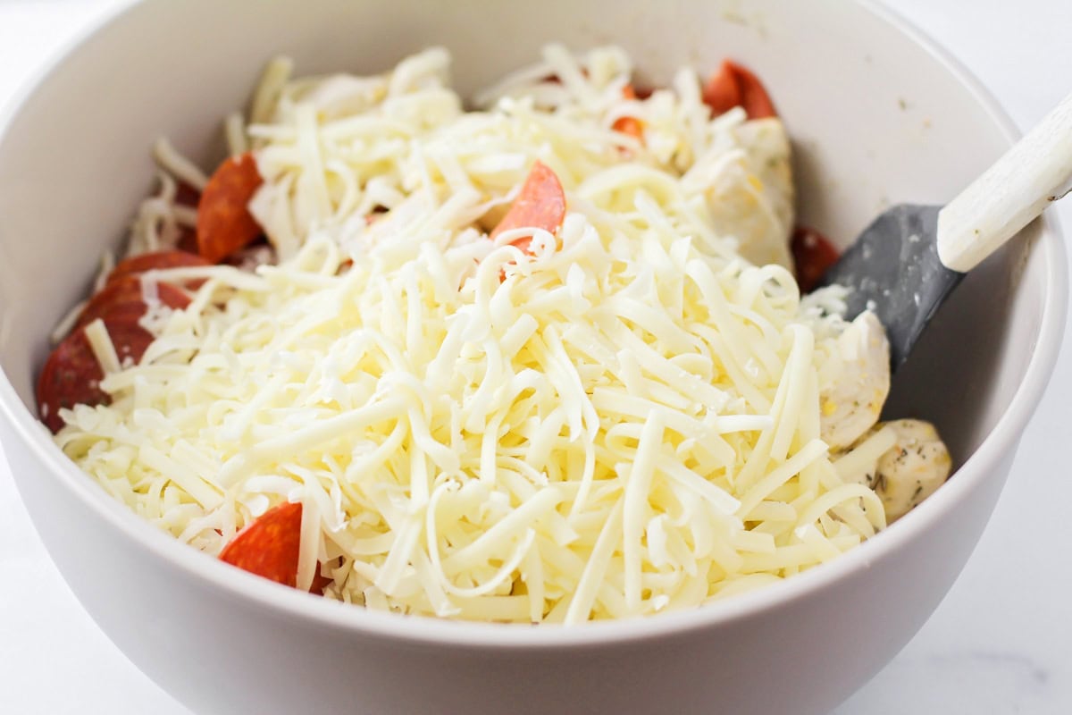 Mixing cheese and pepperoni in a white bowl.