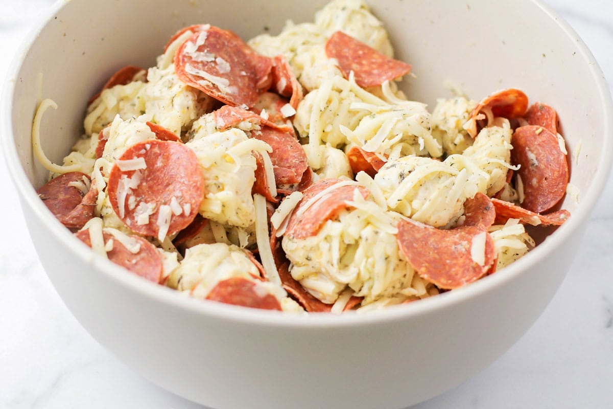 Combining biscuits, pepperoni, and cheese in a white bowl.