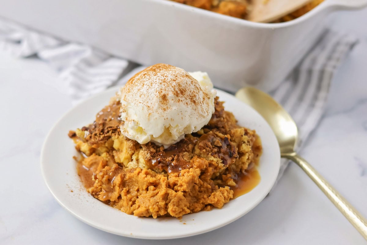 Pumpkin cobbler served on white plate with caramel sauce and ice cream.