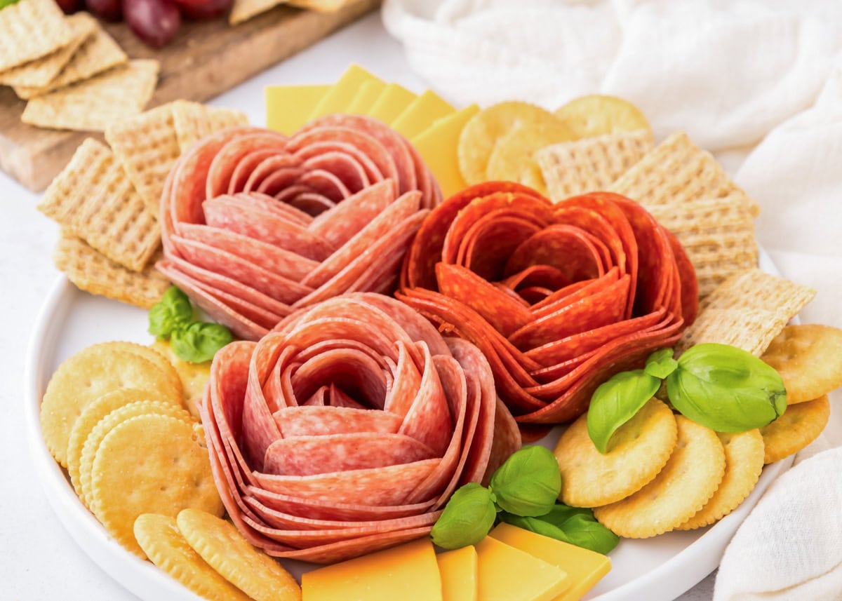 Close up of a salami rose served with crackers and cheese.