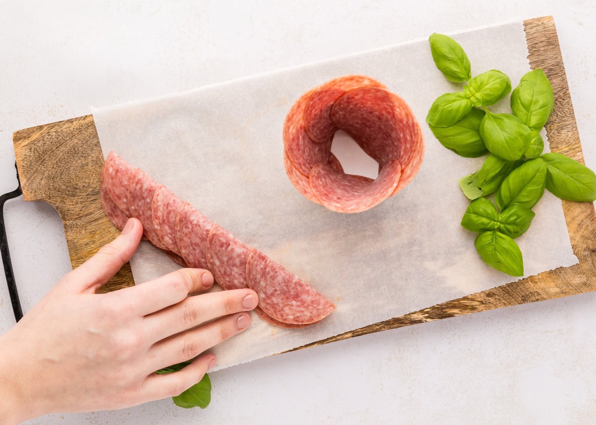 Folding a spread of salami on a cutting board.