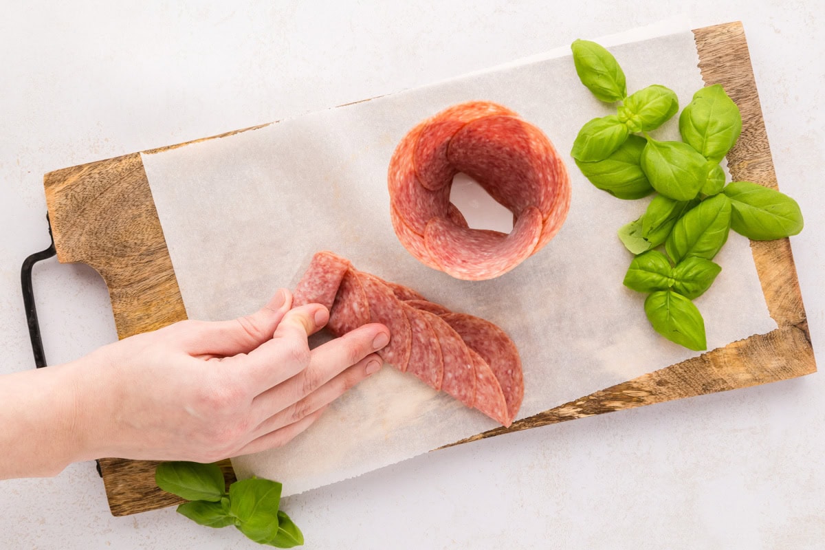 Rolling layered salami on a cutting board.