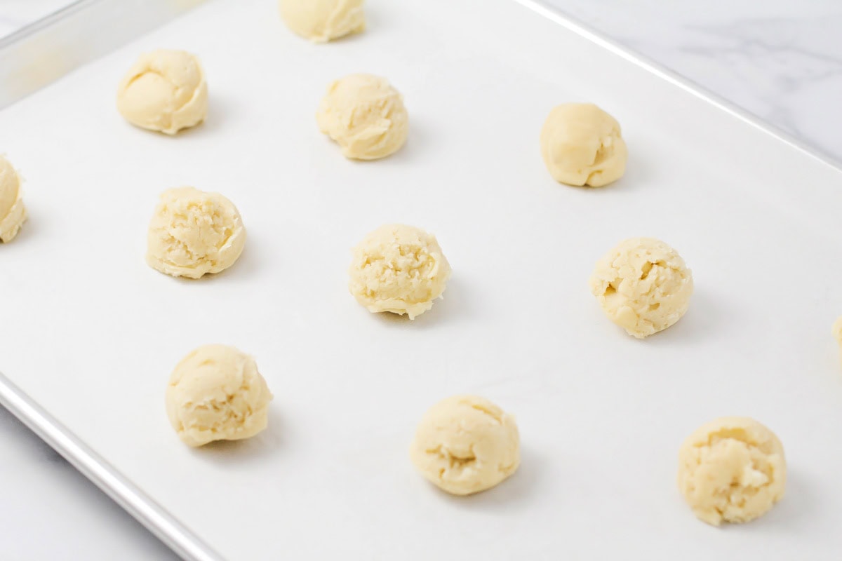 Dropped cookie dough balls on a lined baking sheet.