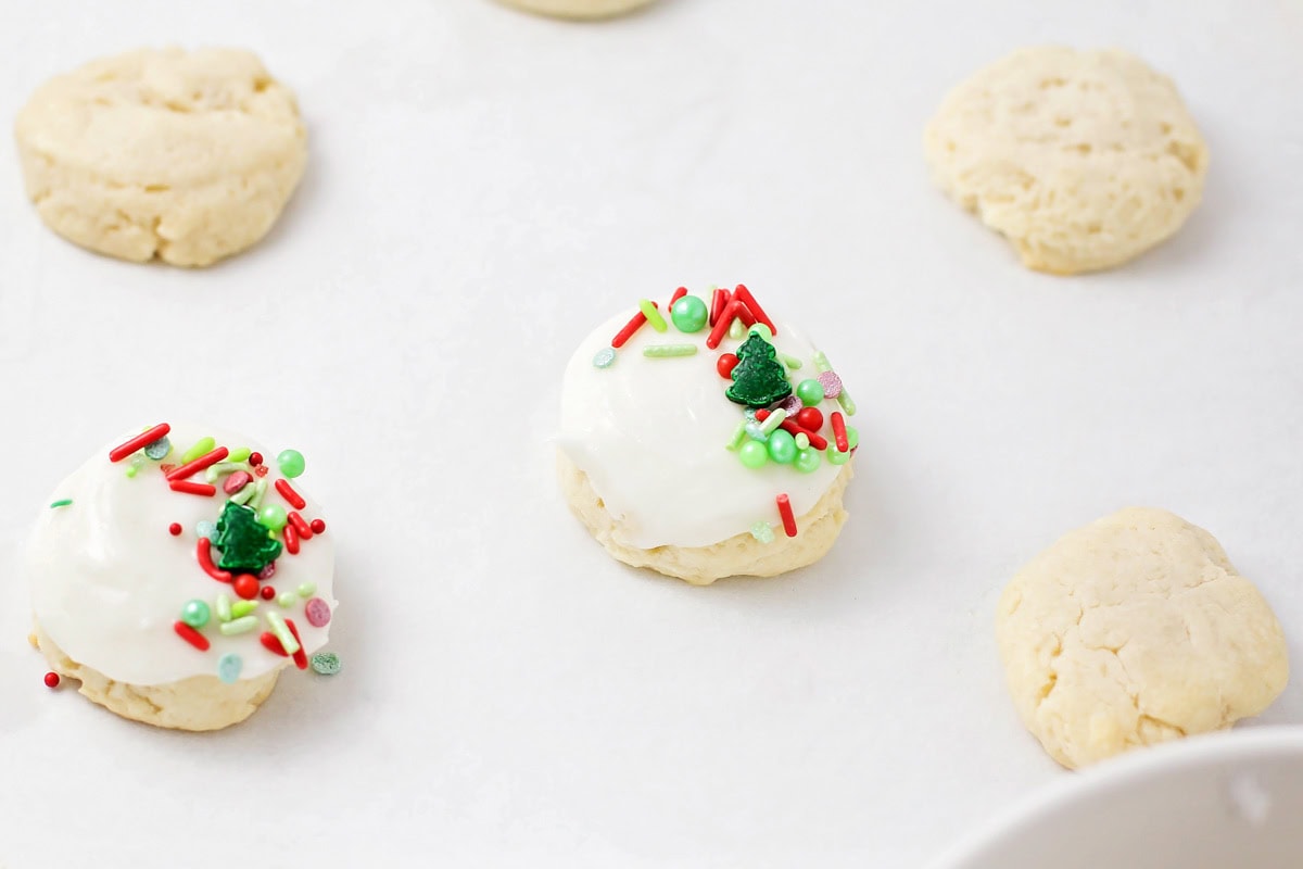 Cookies topped with white frosting and sprinkles.