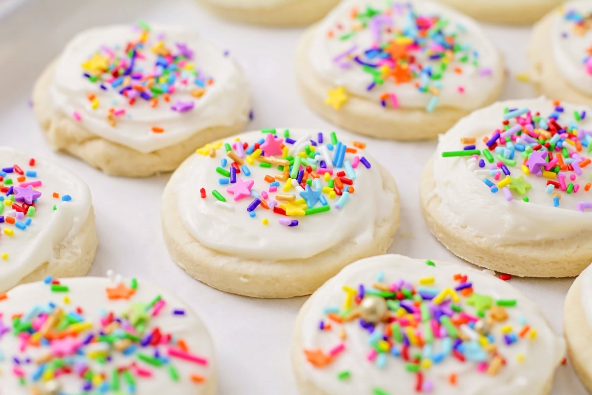 Frosted sugar cookies with white frosting and sprinkles on top.