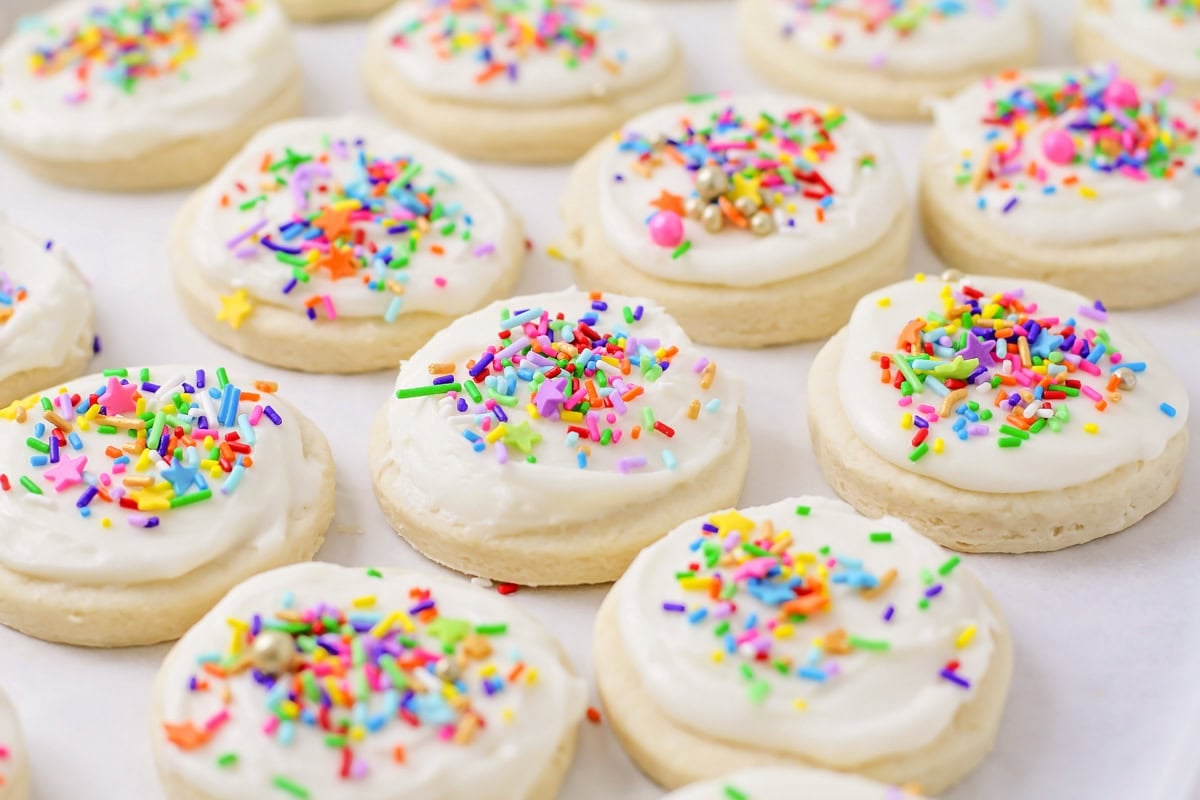 Frosted sugar cookies with sprinkles on parchment paper lined cookie sheet.