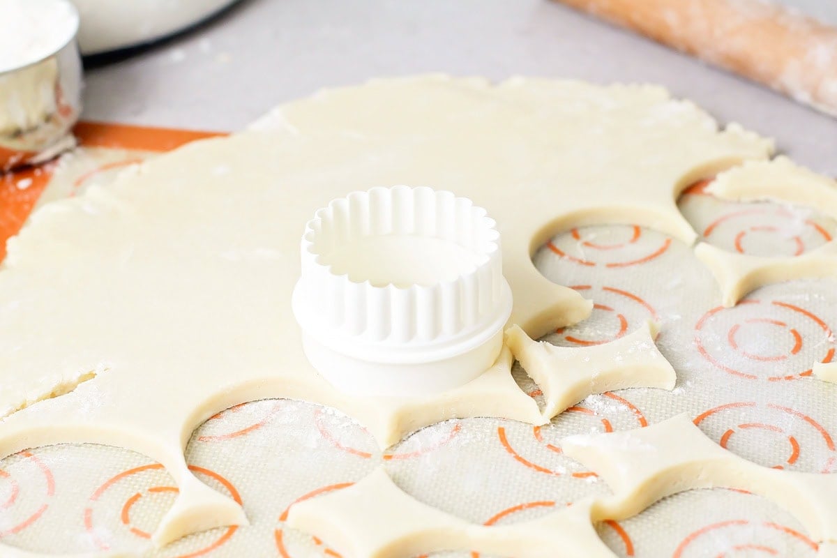 Cookie cutter cutting out dough for frosted sugar cookies.