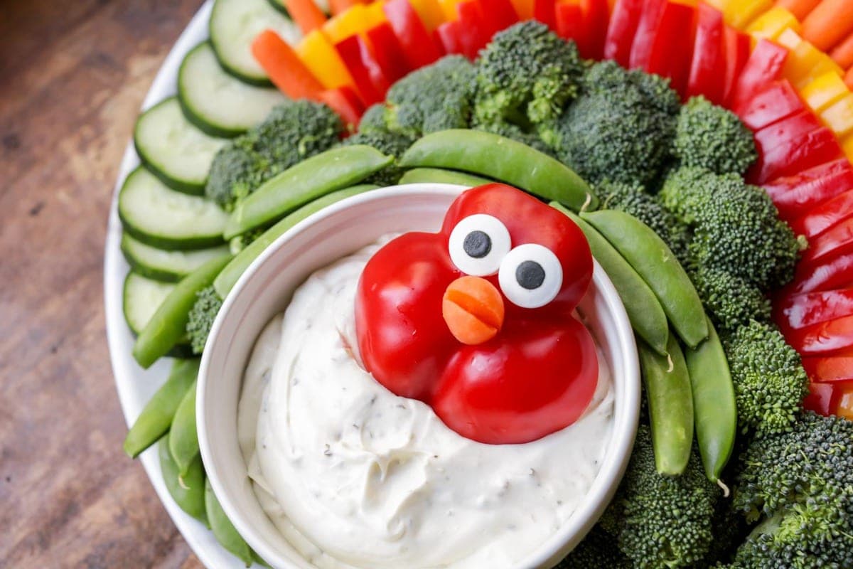 A red bell pepper with eyes and a carrot for mouth surrounded by other raw veggies to resemble a turkey.