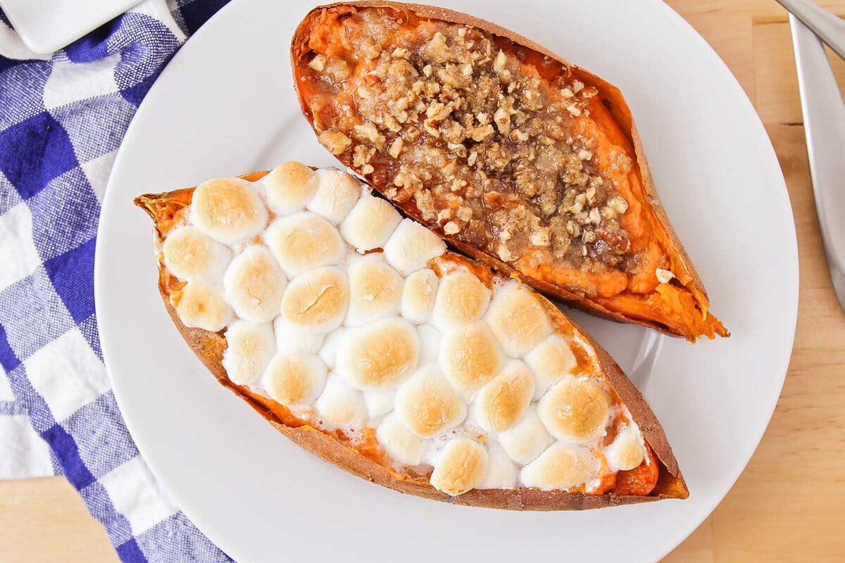 A baked sweet potato split in half with one side covered in browned marshmallows and the other topped with pecan streusel.