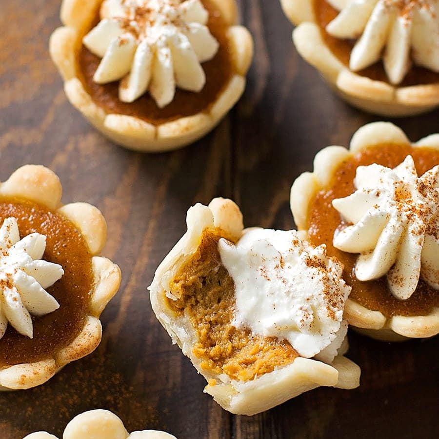 Mini pumpkin pies with whipped cream on top with one mini pie on it's side with a bite taken out of it. 