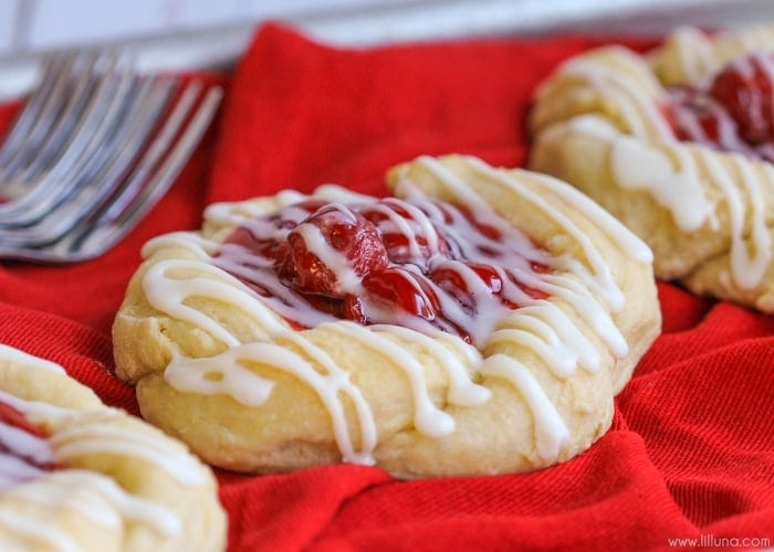 A cherry danish pastry sitting on a red cloth. 