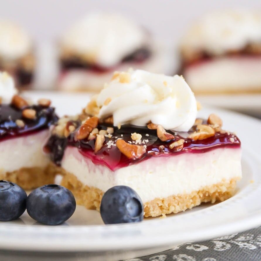 Slice of blueberry delight on white plate with blueberries sprinkled all around.