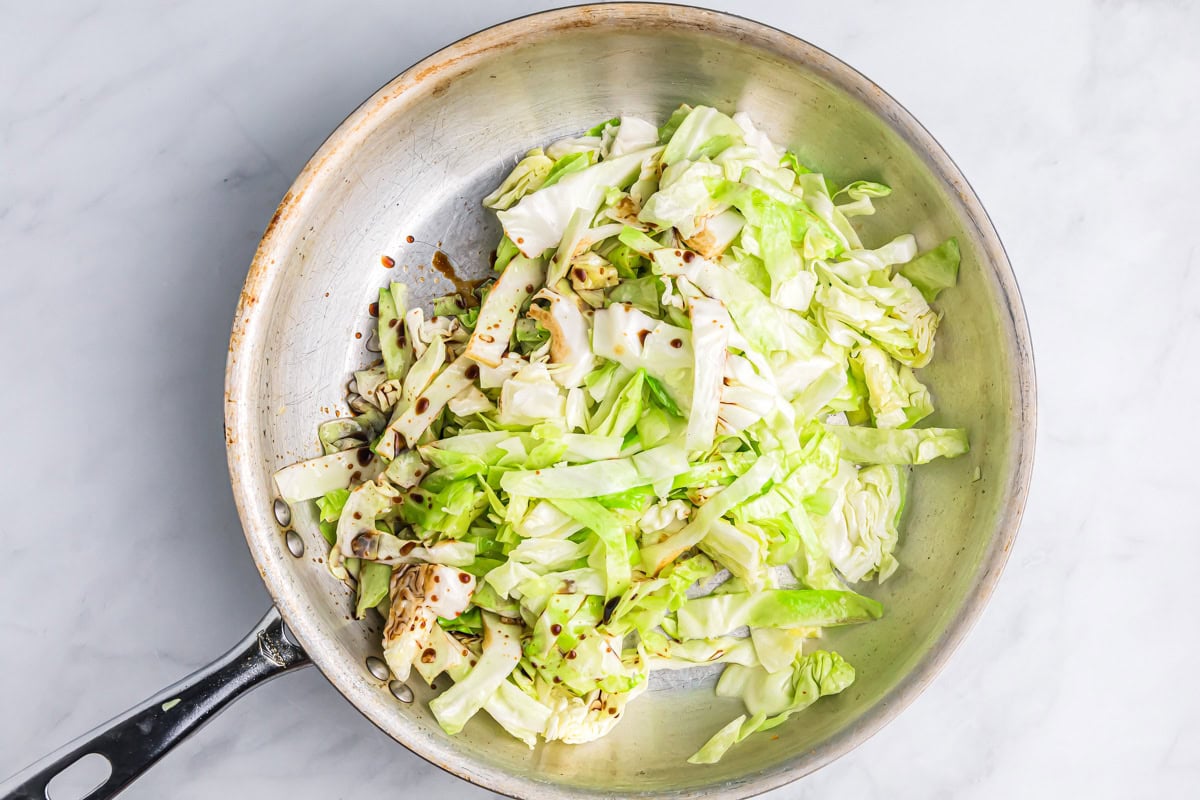 Adding seasonings to a pan of sliced cabbage.