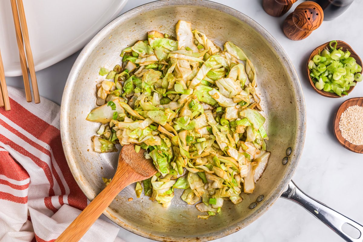 Stirring a pan of cooked cabbage with a wooden spoon.