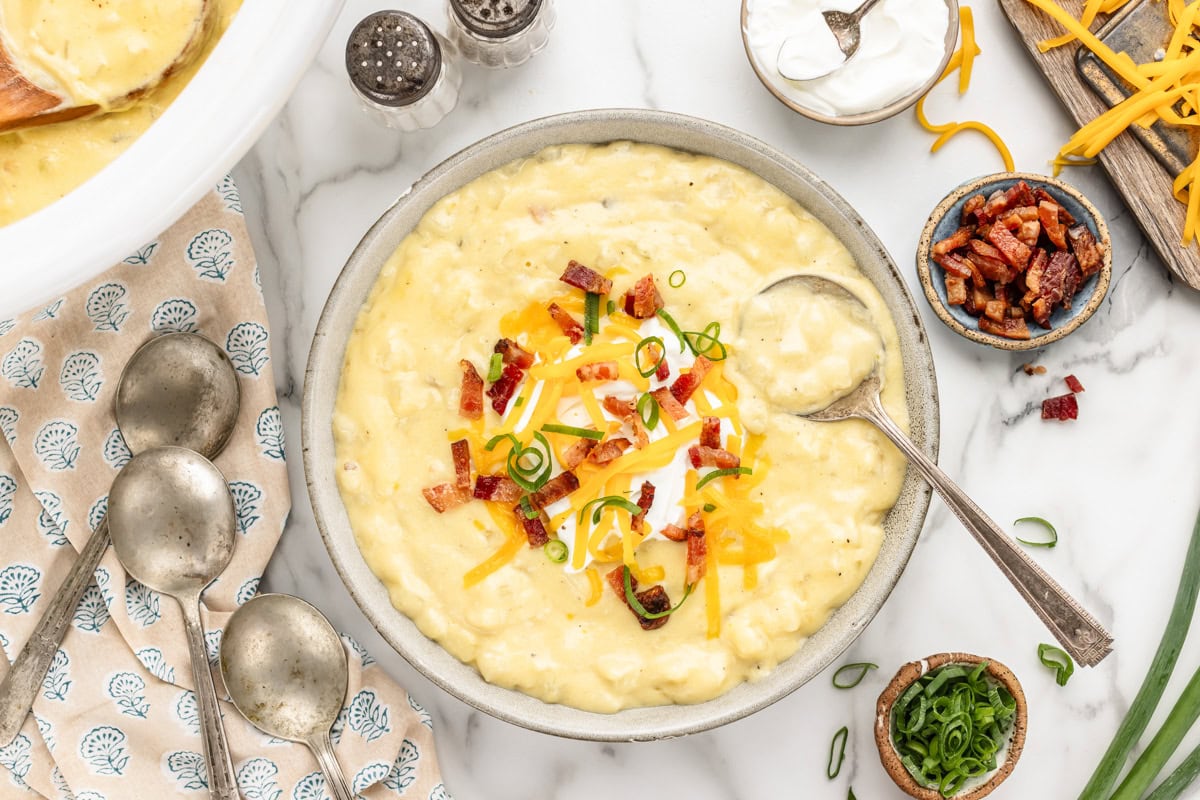 Cheesy potato soup recipe in gray bowl with cheese, bacon and chives on top.