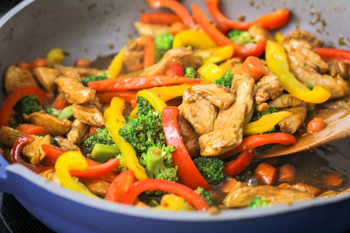 Adding veggies to the chicken cooking in a skillet.