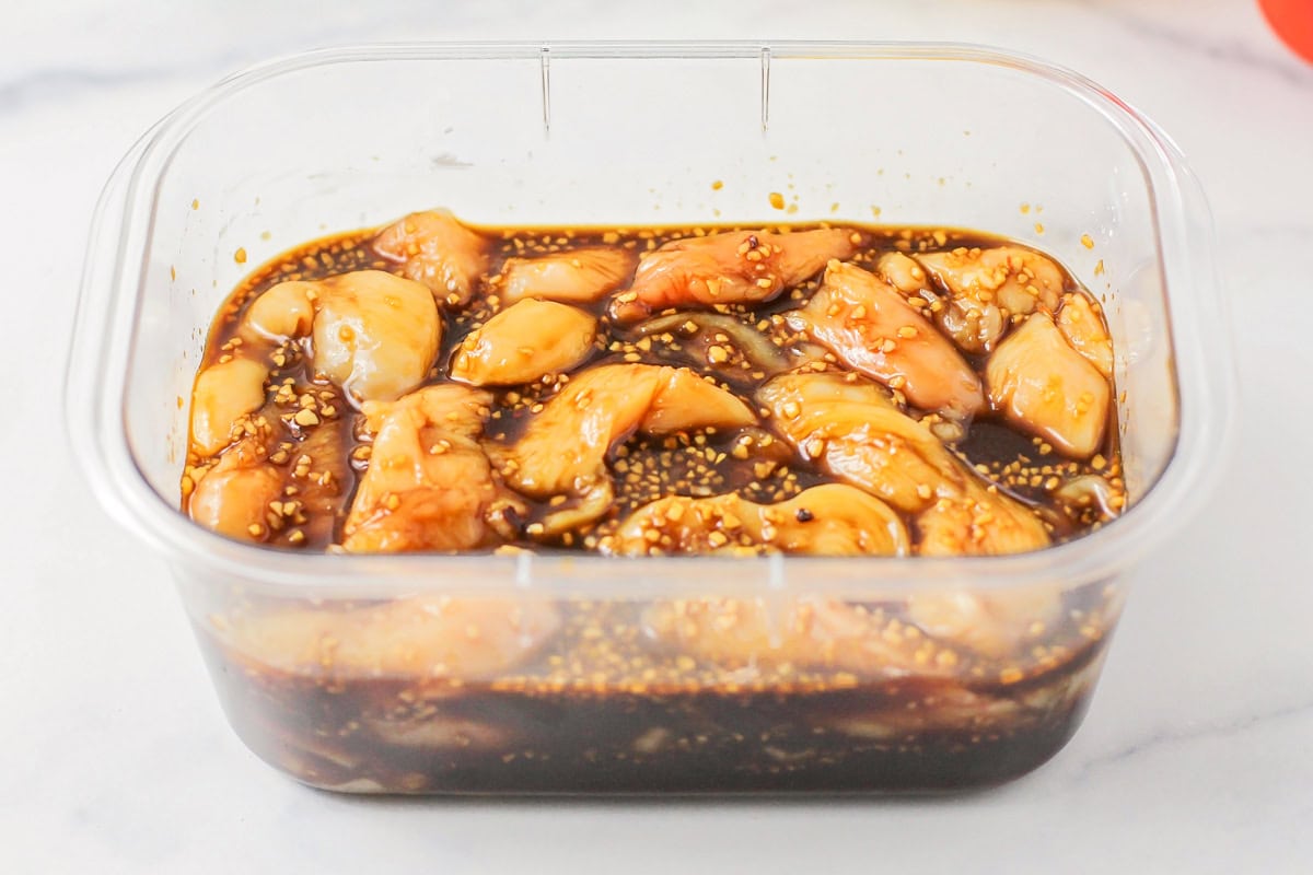 Chicken marinating in a plastic tupperware.