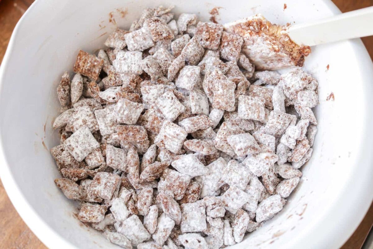 Powdered sugar poured over Christna puppy chow in white bowl.