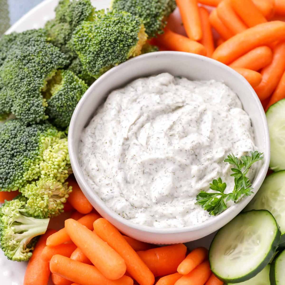 A bowl of veggie dip served with broccoli, carrots, and sliced cucumbers.