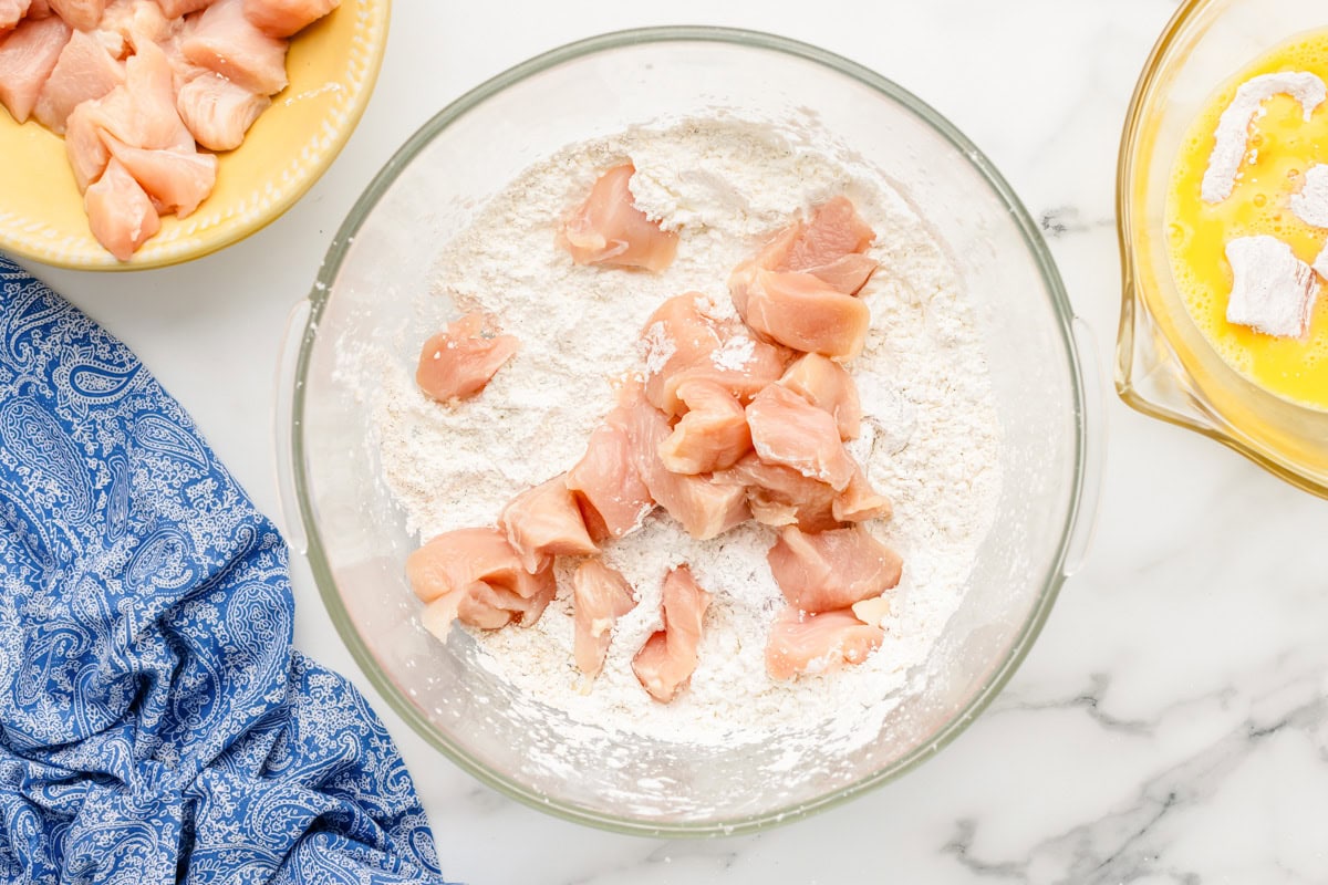 Coating chicken cubes in flour.