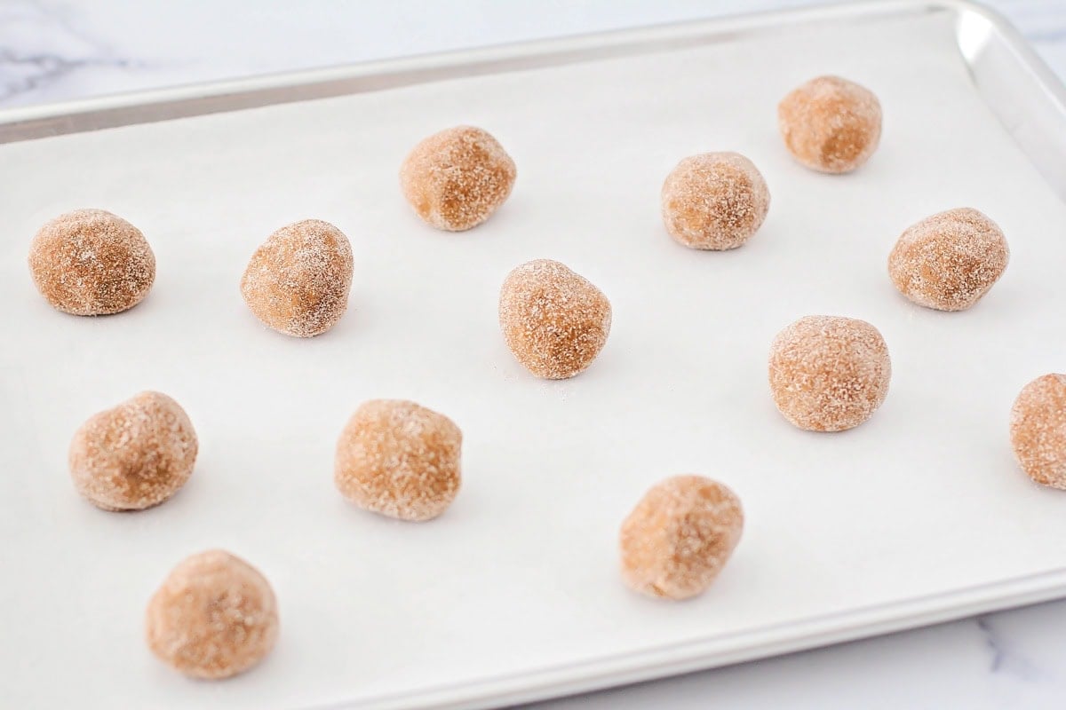 Super soft gingerdoodle cookies are perfectly spiced and coated in a cinnamon sugar mixture for two tasty cookies in one! Gingerdoodle Cookie dough balls on a lined baking sheet.