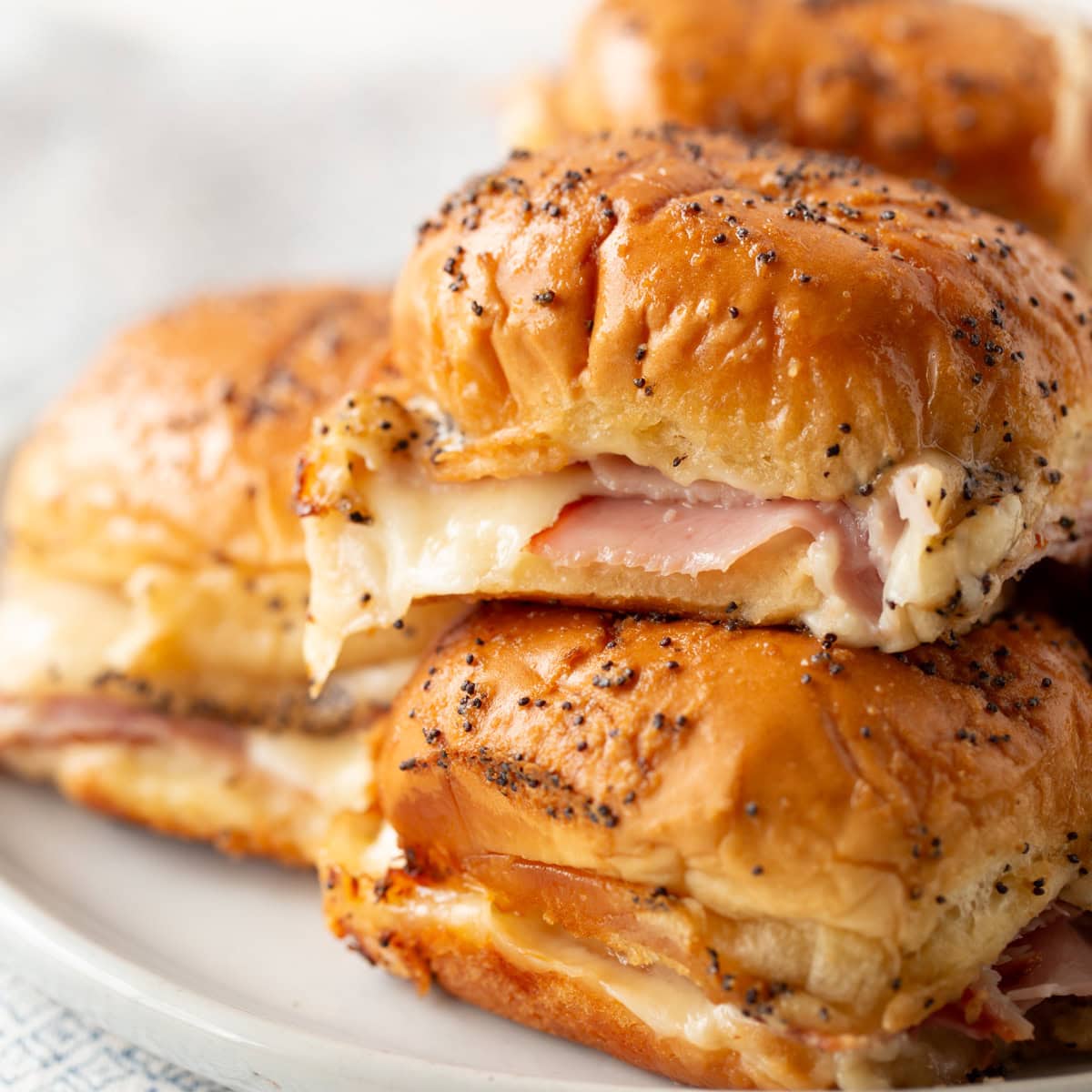 Hot ham and cheese slider recipe close up image - stacked on each other on white plate.