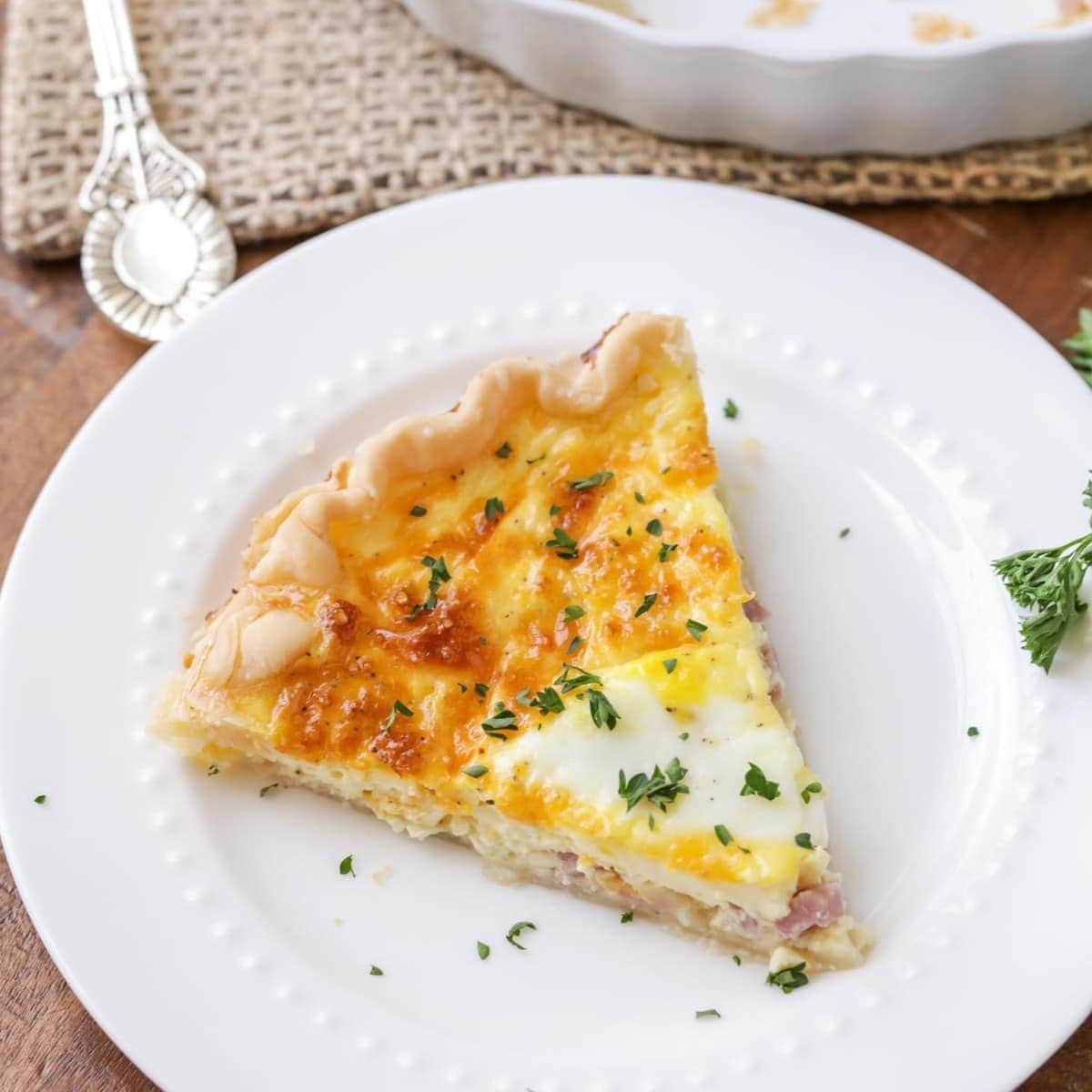 A slice of ham and cheese quiche on a white plate.