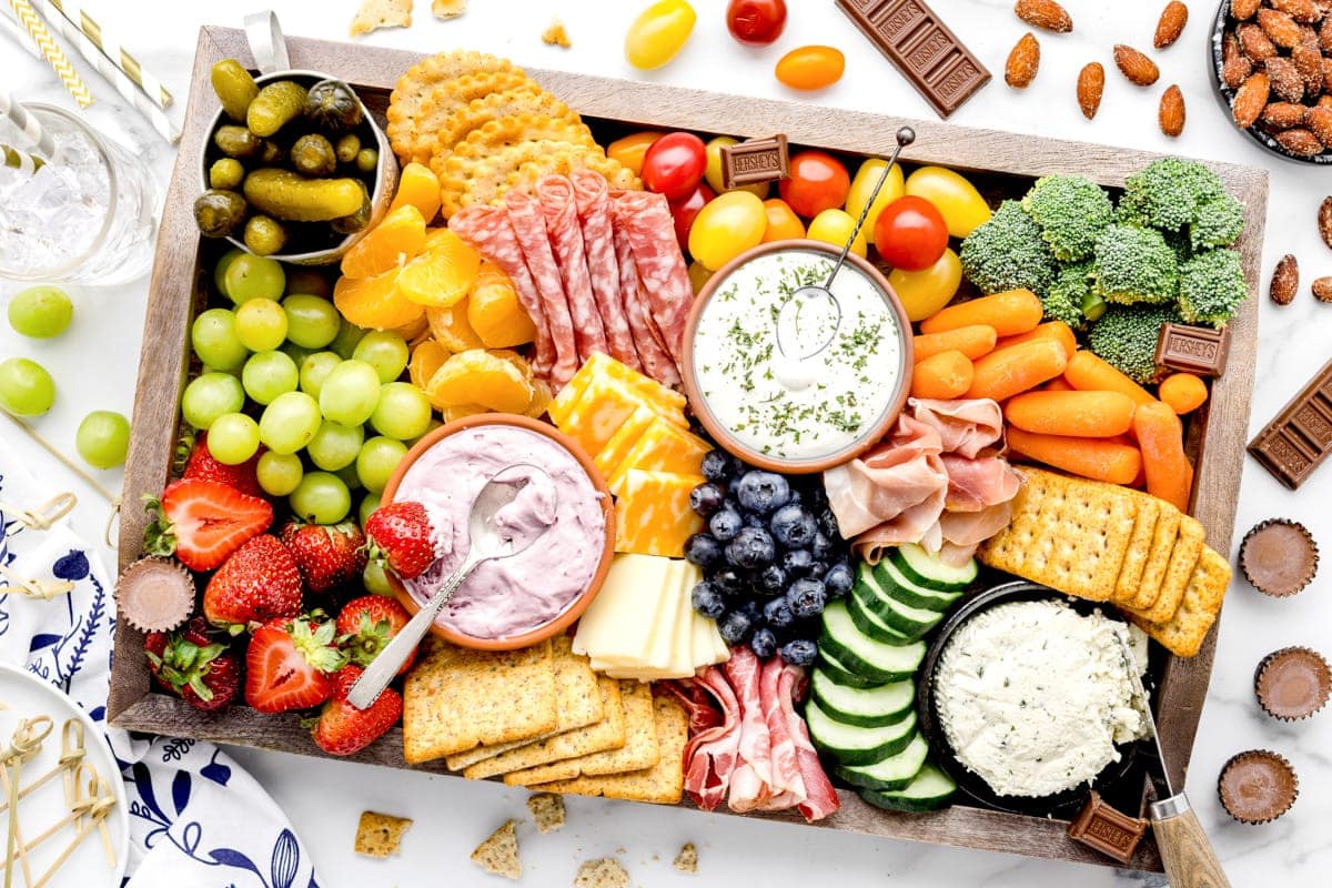 A charcuterie board filled with crackers, veggies, fruits, and dips. 