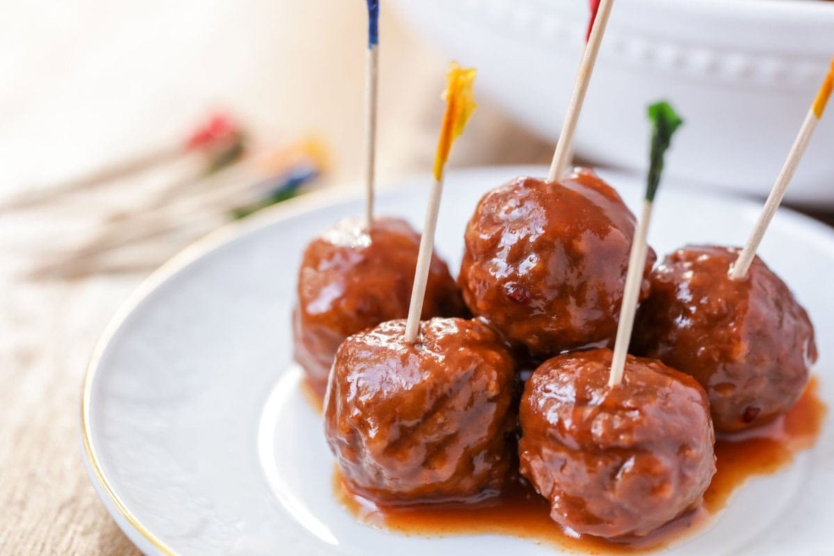 A plate of meatballs covered in sauce with toothpicks for serving. 