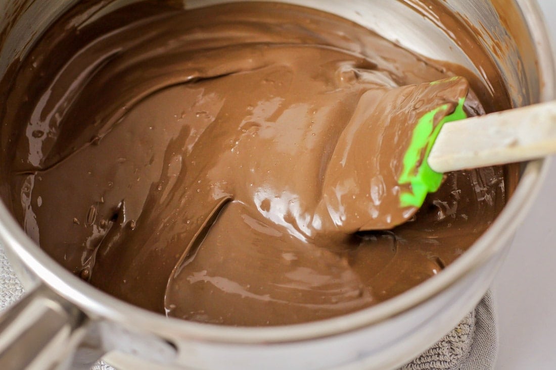 Mixing melted chocolate in a metal mixing bowl with a silicon spatula.