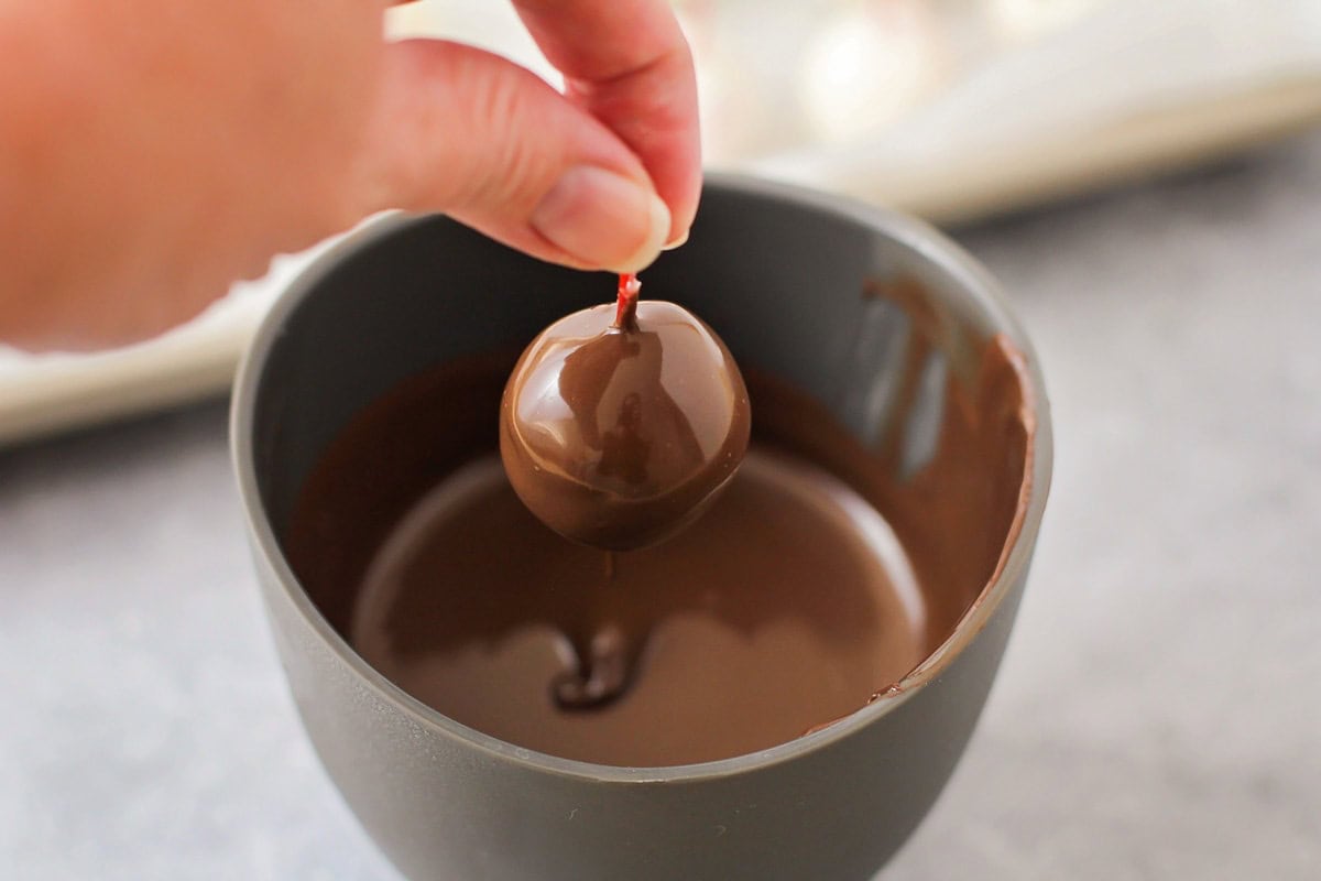 Dipping a cherry into melted chocolate.