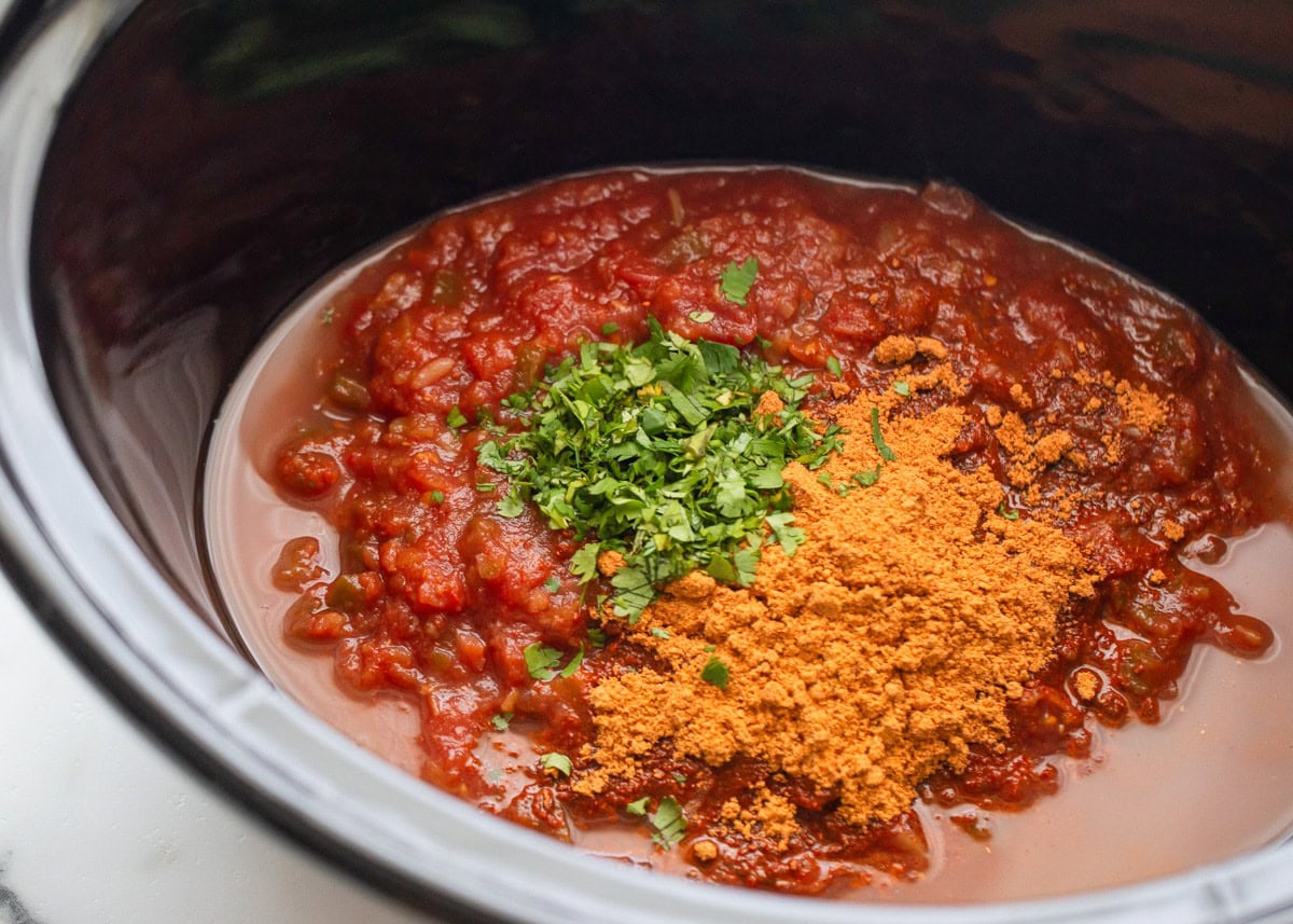 A red tomato sauce being cooked in a slow cooker with seasonings just added on top. 