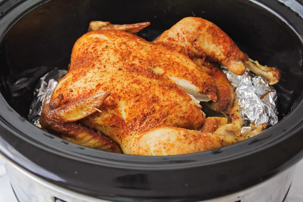 A whole roasted chicken in a crock pot with foil on underneath the chicken. 