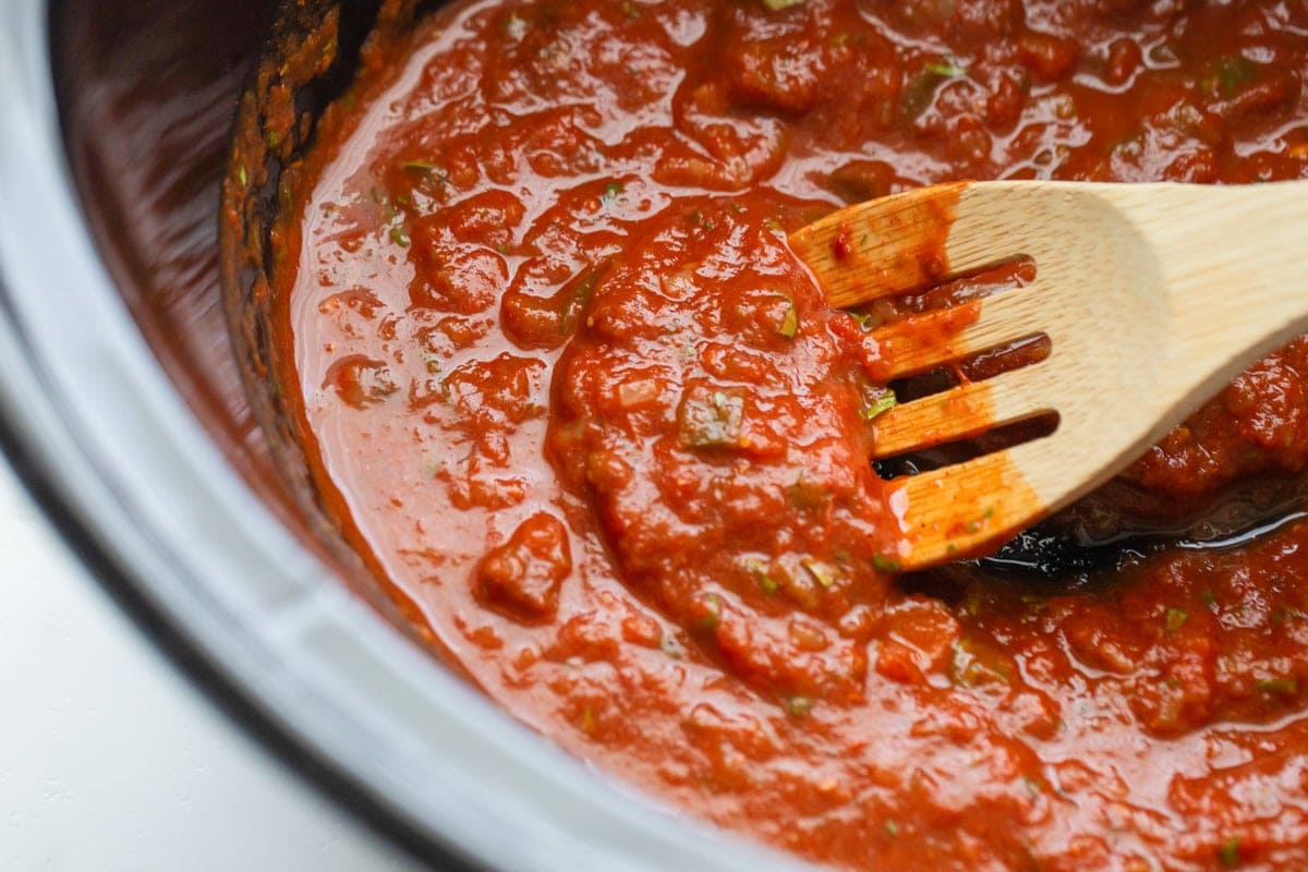 A close up of red sauce being stirred in a crock pot. 