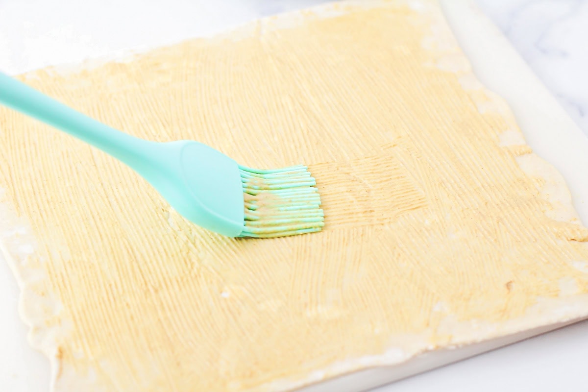 Spreading mustard on a sheet of puff pastry.