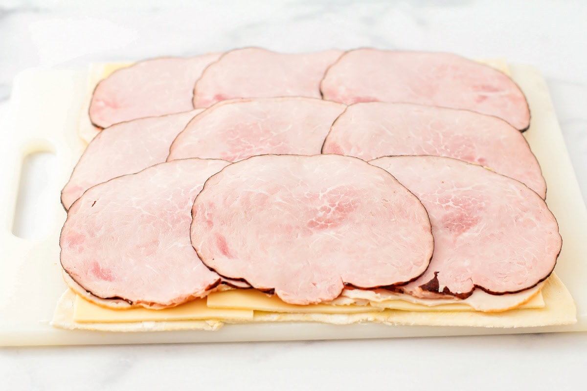 Layering ham, turkey, and cheese on a sheet of puff pastry.