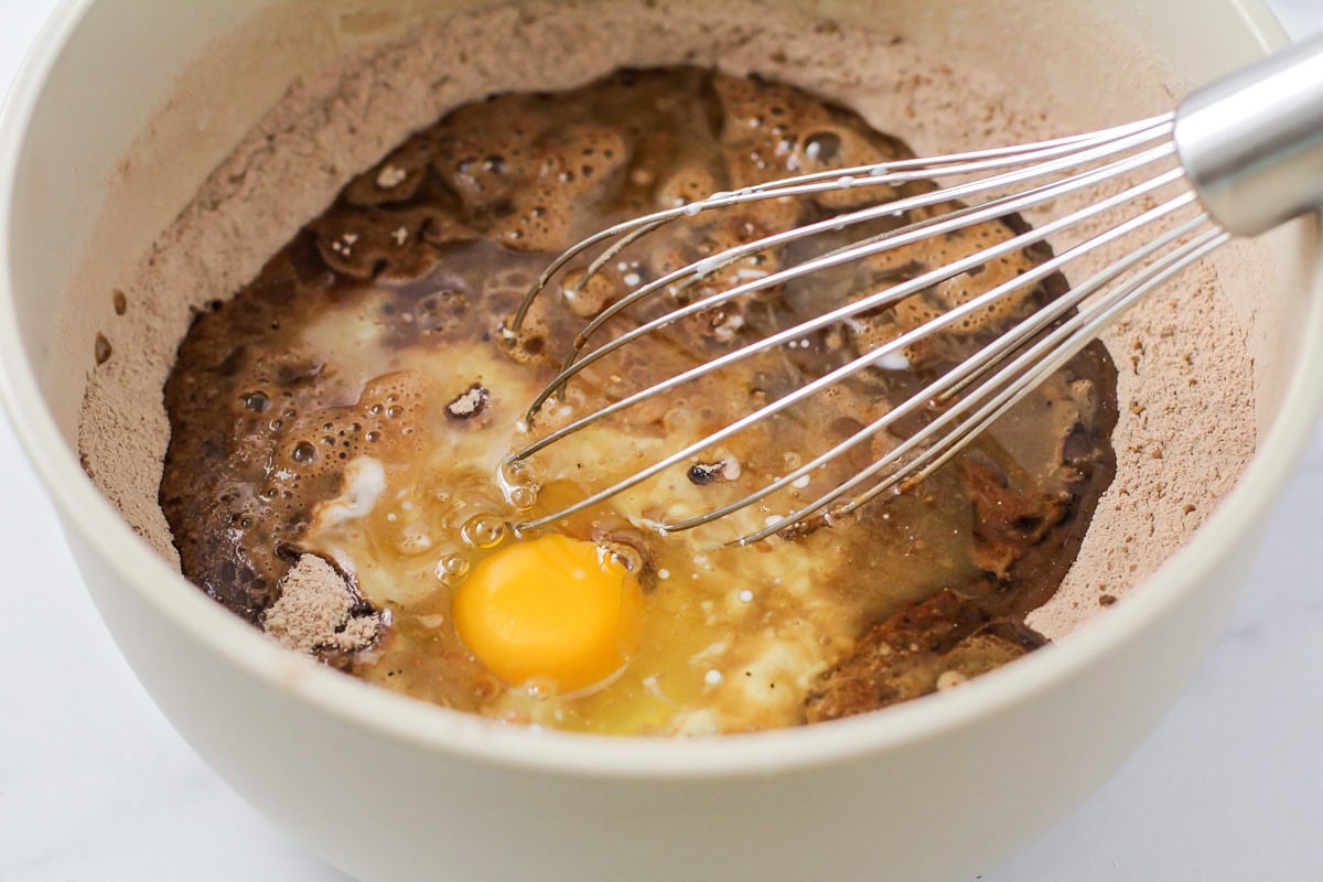 Adding wet ingredients to dry ingredients in a white bowl.