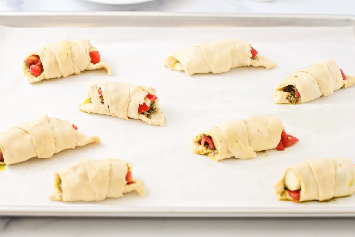 Wrapped and filled croissants on a lined baking sheet.