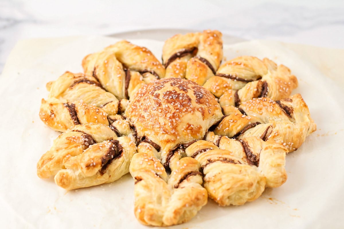 A golden brown puff pastry snowflake on a lined baking sheet.