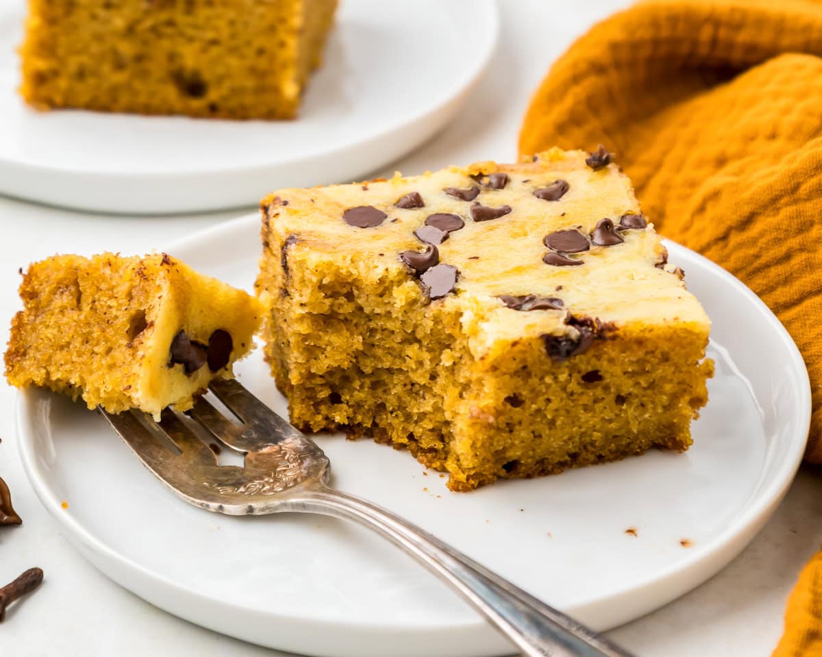 Fork and piece of pumpkin cream cheese bar on white plate.