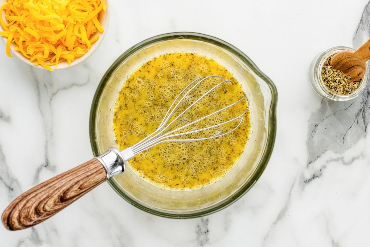 Whisking eggs and seasonings in a glass bowl.