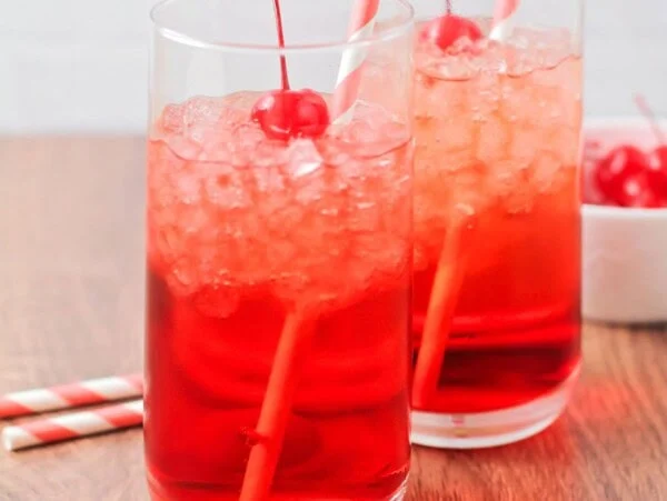 Shirley temple drink image with straws, ice and cherries in the cups.